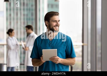 Happy handsome doctor man in blue uniform holding digital tablet Stock Photo