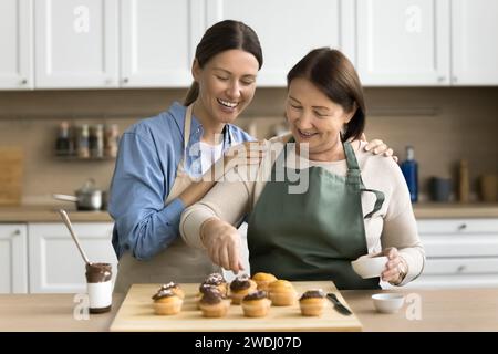 Cheerful confectioner mom and adult daughter woman decorating homemade cupcakes Stock Photo
