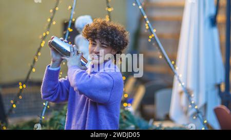 caucasian young cool red haired barista mixing a a cocktail in shaker with energy outdoors in private event in winter time Stock Photo