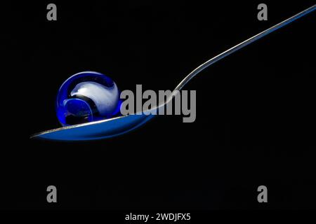 A blue glass swirl marble in a spoon. Stock Photo