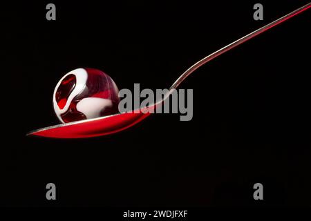 A red glass swirl marble in a spoon. Stock Photo