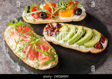 Set of open toasted bruschetta with arugula, jamon, vegetables, cream cheese close-up on a slate board on the table. Horizontal Stock Photo