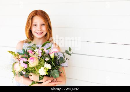 Close up portrait of adorable red hair kid girl holding big flower bouquet with roses Stock Photo
