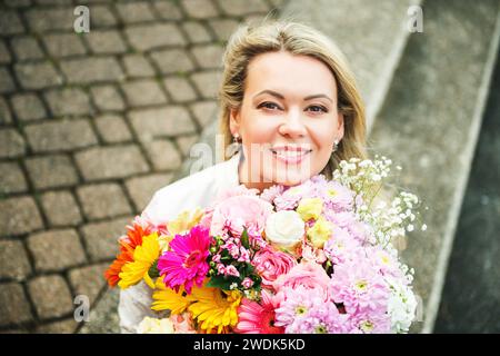Outdoor close up portrait of blond woman holding big bouquet of nice fresh flowers Stock Photo