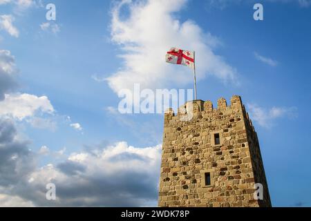 National flag of Georgia on the top of old stone tower flies waving against the background of a blue sky with clouds. Rabat Fortress, Akhaltsikhe. Tra Stock Photo