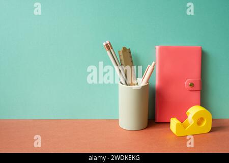 Pink diary notebook and writing supplies stationery in holder on red desk. mint green wall background Stock Photo