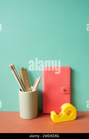 Pink diary notebook and writing supplies stationery in holder on red desk. mint green wall background Stock Photo