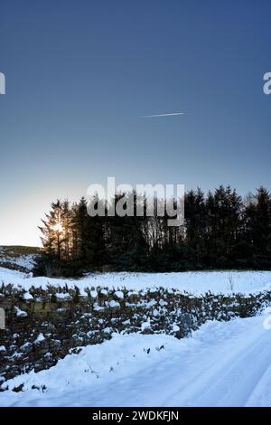 Against a clear, blue sky, a jet plane leaves a vapour trail in January  the day after a sudden fall of snow. Nidderdale. North Yorkshire. Stock Photo