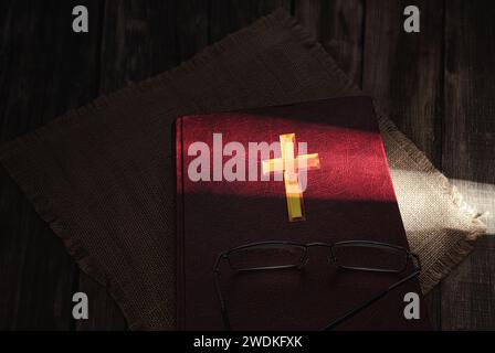 A book and glasses on which a ray of sunlight falls. Bible book on a wooden background. A ray of sunshine pierces the darkness. Stock Photo