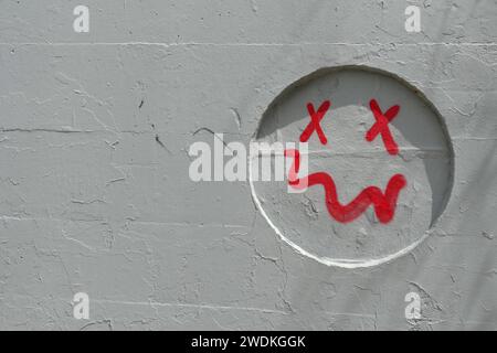 Simple smiling face with crooked mouth spray painted on gray wall recess. Abstract background. Stock Photo