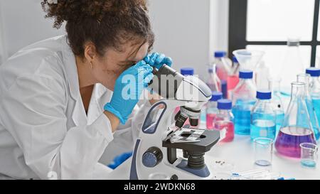 Hispanic woman with curly hair using microscope in laboratory Stock Photo
