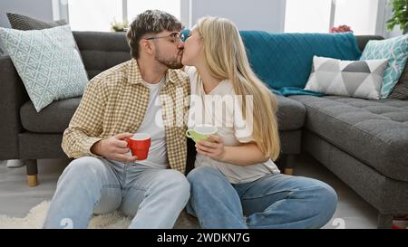 A loving couple shares a kiss on the floor of a cozy living room, each holding colorful mugs, in a casual home setting. Stock Photo