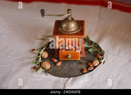 Retro coffee grinder on table with nuts and olive branch over beautiful old linen tablecloth Stock Photo
