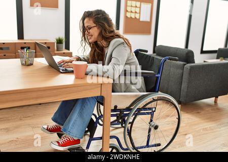 Young beautiful hispanic woman business worker using laptop sitting on wheelchair at office Stock Photo