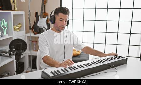 Attractive young hispanic man, a talented musician, immersing himself in the melody, passionately playing the acoustic piano wearing headphones in a l Stock Photo
