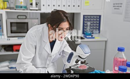 A mature hispanic woman scientist examines samples using a microscope in an indoor laboratory setting. Stock Photo