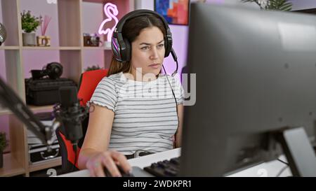 Focused young woman with headphones using a computer in a modern gaming room at night. Stock Photo