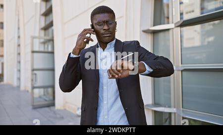 African american businessman in suit checking time while talking on phone against urban background Stock Photo