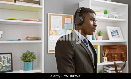 African american man wearing headset in modern office setting listening attentively during a workday. Stock Photo