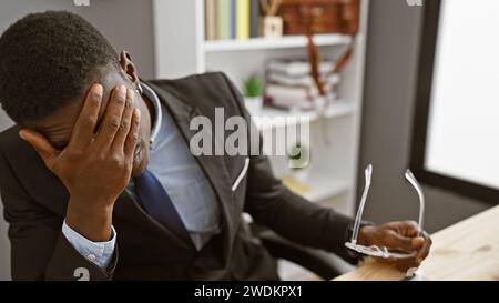 Tired african american businessman in office holding glasses, with hands on face showing stress or headache. Stock Photo