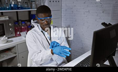 African american scientist in lab coat and safety goggles uses a computer in a modern laboratory setting. Stock Photo