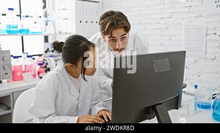 A man and woman work together in a laboratory, looking intently at a computer screen amidst scientific equipment. Stock Photo
