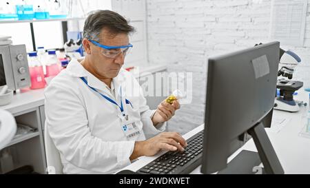 Mature man in lab coat examines medication bottle in bright laboratory while using computer. Stock Photo