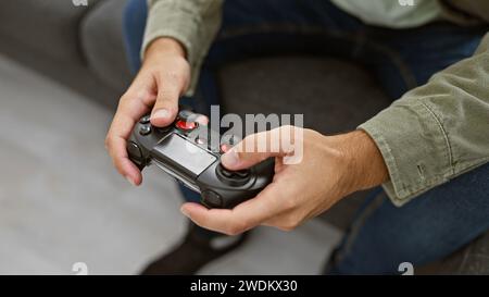 A focused young man enjoys gaming with a controller in a cozy living room setting at home. Stock Photo