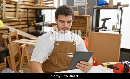 Young bearded man using a tablet in a carpentry workshop, reflecting a busy creative professional at work. Stock Photo