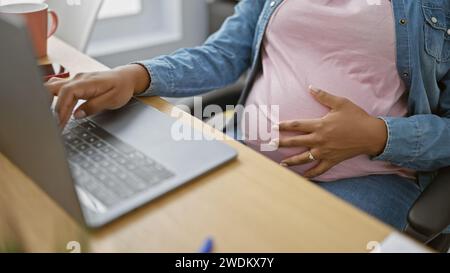 Expecting a bundle of joy, our young latin businesswoman finds success in work, massaging her pregnant belly while mastering technology on her laptop Stock Photo