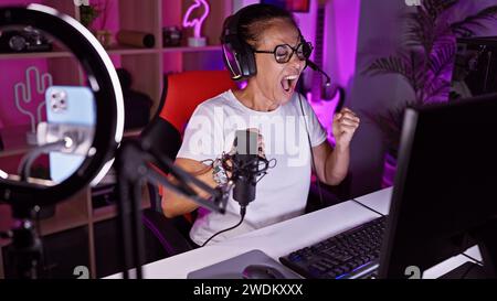 Excited woman gaming indoors at night in a home office with vibrant led lights, showcasing technology and entertainment. Stock Photo