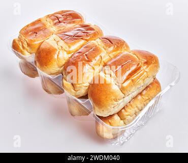 Close-up of fresh, golden-brown dinner rolls in a plastic tray against a white background. Stock Photo