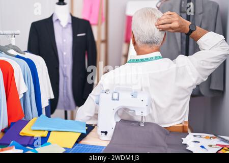 Middle age man with grey hair dressmaker using sewing machine backwards thinking about doubt with hand on head Stock Photo