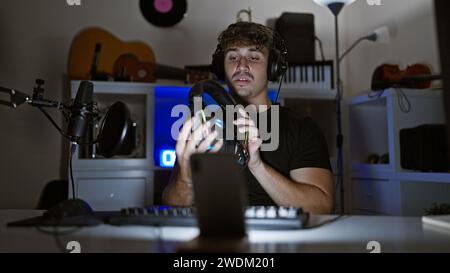 Handsome hispanic man caught in thrilling night-time gaming stream, engrossed in virtual conversation amidst the glow of his gaming room, headphones r Stock Photo