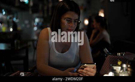 Young beautiful hispanic woman using smartphone sitting on the table at the restaurant Stock Photo