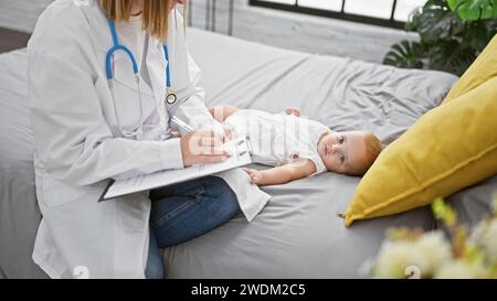 Pediatrician in uniform, patiently sitting on a bedroom bed, seriously examining baby, meticulously taking medical notes indoors Stock Photo