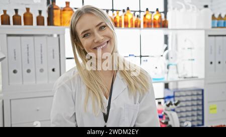 Bright and confident young blonde woman scientist, beautifully smiling, enjoying her work standing in laboratory, immersed in medical research Stock Photo