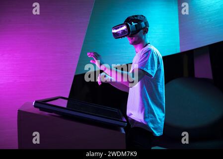 Young man interacting in a digital world, using virtual reality headset with motion tracking tech, making hand gestures in the air. Stock Photo