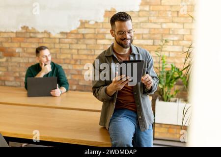 In a contemporary office setting, two focused colleagues engage in their work with tablet and laptop, collaborating and sharing ideas in a bright and Stock Photo