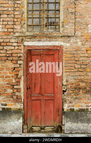Old red door in a medieval red brick wall with window with cross bars above, Palazzo Reale, Turin Italy Stock Photo