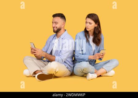 Man and woman sitting back-to-back, focused on their smartphones Stock Photo