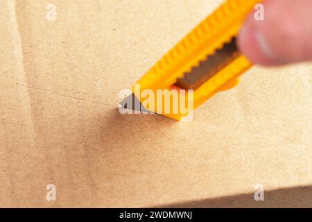 Unboxing parcel box. Opening cardboard package with utility knife. Cutting brown kraft paper close up Stock Photo