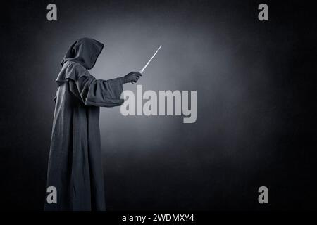 Wizard with hooded cape and magic wand over dark misty background Stock Photo