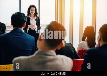 Office meeting with a diverse group of businesspeople. Seated colleagues converse, while male and Stock Photo