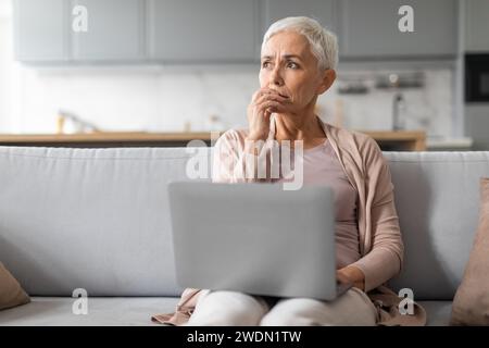 Concerned mature lady working on laptop thinking about issues indoor Stock Photo