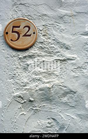 Portrait format close up shot of a number 52 plaque on a rough textured rendered wall. Stock Photo