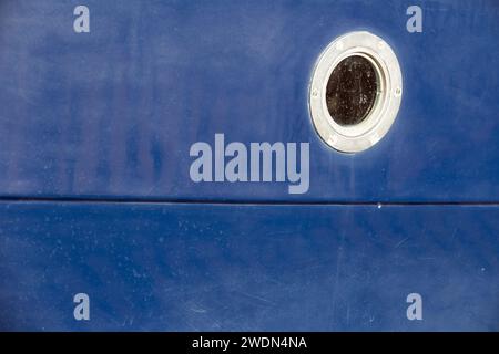 A close up shot of a dark blue boat showing the side of the boat filling the frame and including a single port hole. Stock Photo