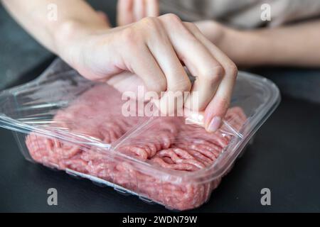 A hand opens a pack of fresh minced meat close-up. The process of cooking tasty cutlets. Stock Photo