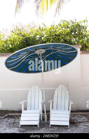 Two empty white deck chairs under an umbrella. Stock Photo