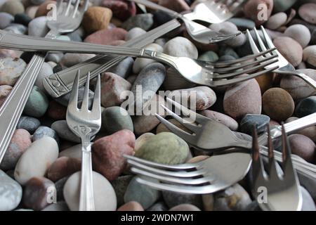 Identical table forks and cake forks from the cutlery set lying on small smooth sea rocks Stock Photo